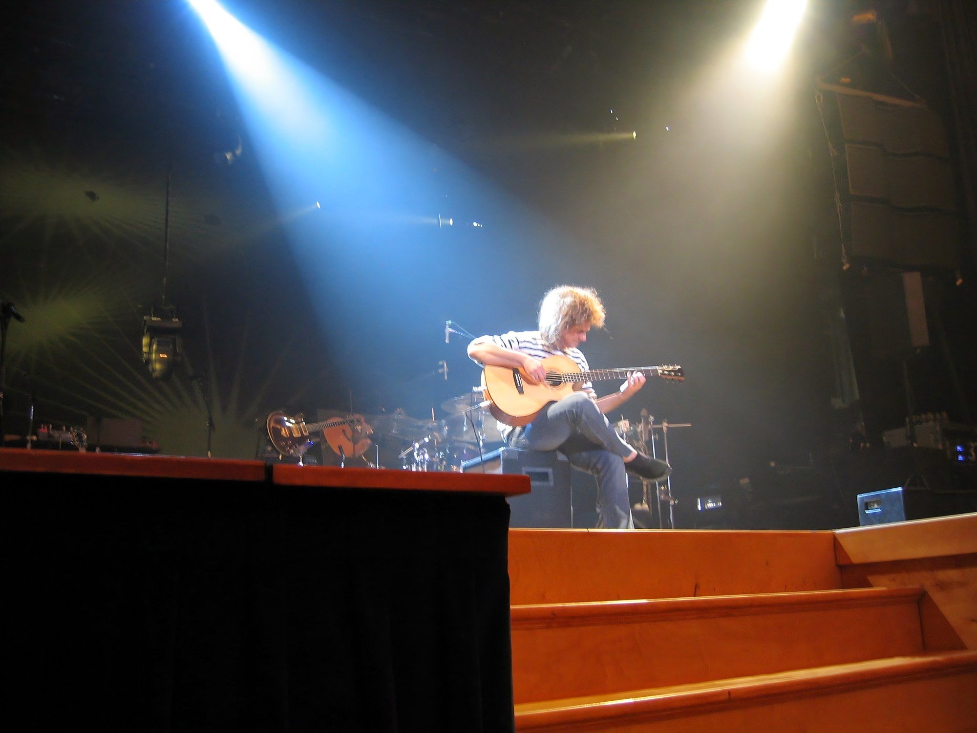 Pat Metheny alone on stage with an acoustic guitar under a blue-white spotlight