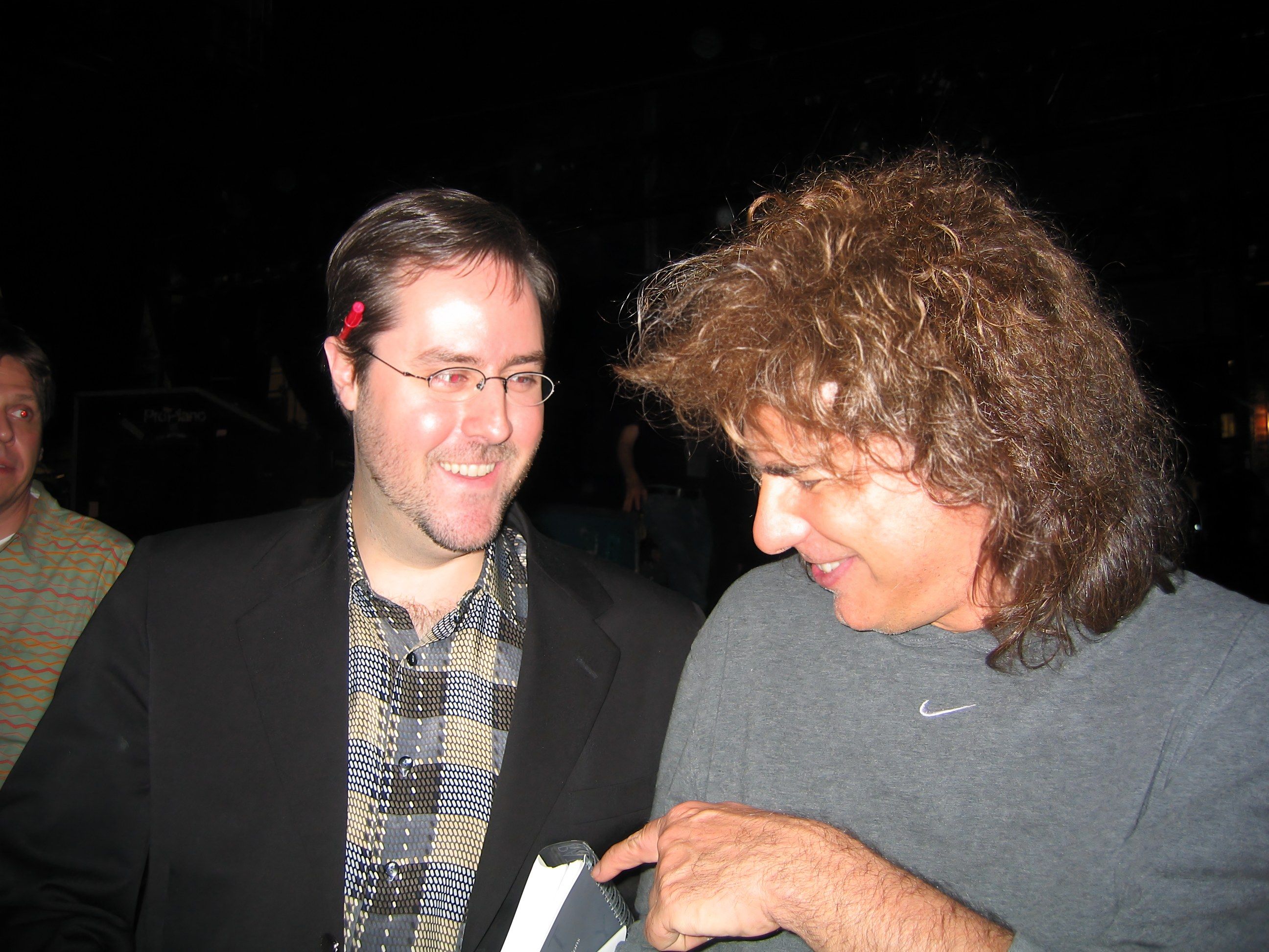 Pat Metheny, in a grey T-shirt and holding a bound copy of Sean’s dissertation, leans toward Sean Fenlon, in glasses and a dark jacket, backstage at Lisner Auditorium