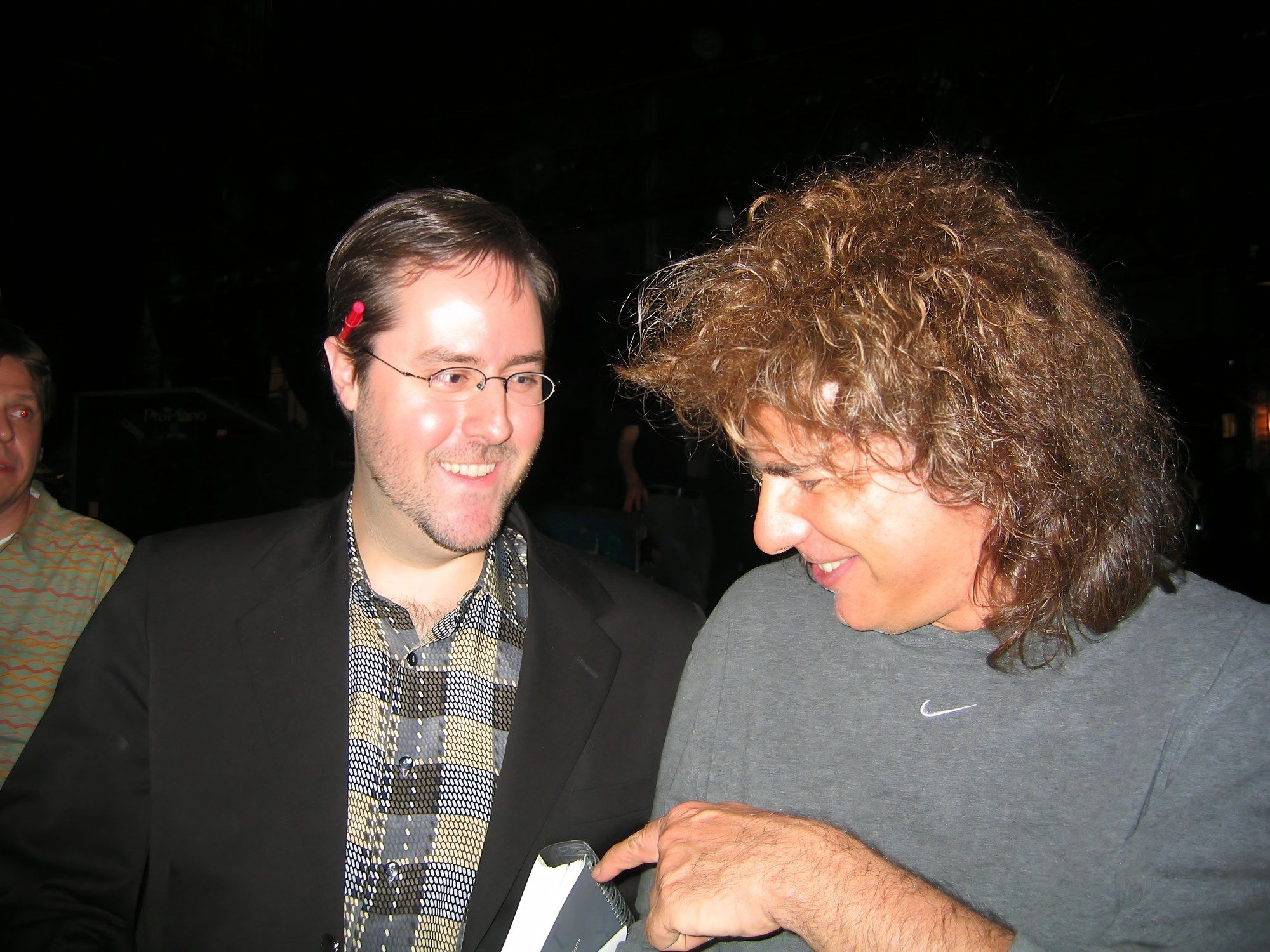 Pat Metheny, in a grey T-shirt, leans toward Sean Fenlon, in glasses and a dark jacket, backstage at Lisner Auditorium