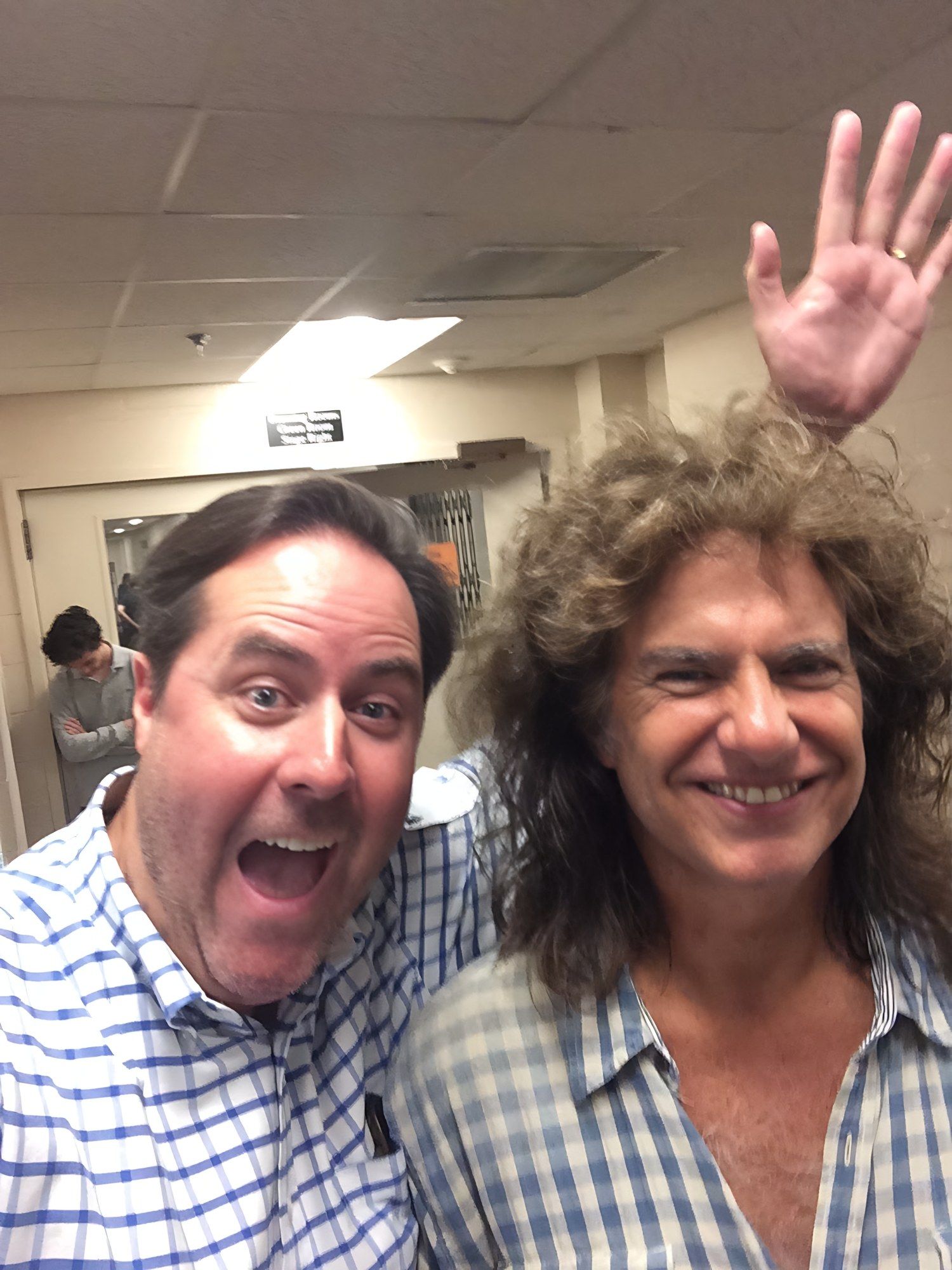 Selfie of Sean Fenlon, in a blue gingham shirt, and Pat Metheny, smiling and waving, in a backstage corridor